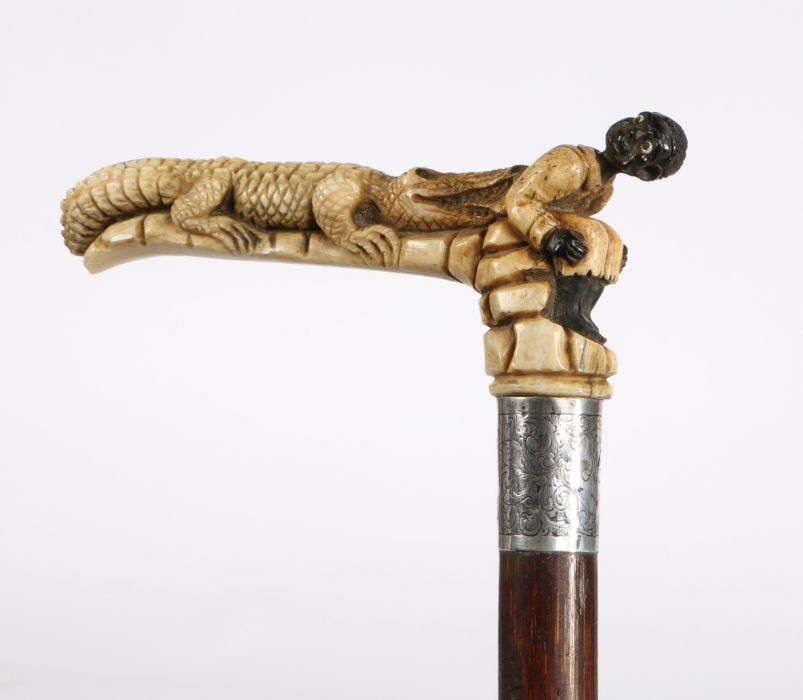A late 19th century walking cane with bone handle depicting an alligator biting a young boy on the