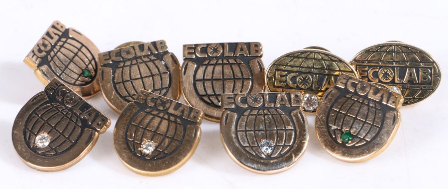 Nine Ecolab presentation badges set with mostly clear stones, stamped 1/10 10k, weight 40.7 grams