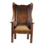 A George III joined oak 'lambing-type' wing armchair, circa 1760 Having a panelled back, ogee-