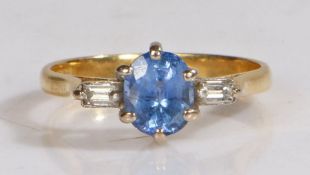 An 18 carat gold and tanzanite set ring, the central round cut tanzanite with a diamond to either