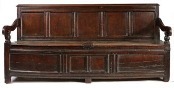 A George III oak settle, the back with five panels and flanked by two shaped arms on turned