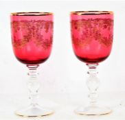 Pair of cranberry and gilt decorated wine glasses, with floral garland decoration, 18cm tall,