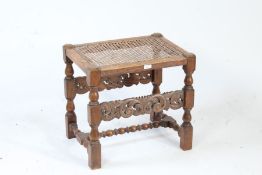 A 20th century oak stool, set with a cane top above turned legs and pierced scroll frieze, 51cm wide
