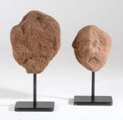 A pair of primitive carved stone archaic heads Each on a metal stand, 30cm & 25cm tall including