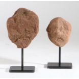 A pair of primitive carved stone archaic heads Each on a metal stand, 30cm & 25cm tall including