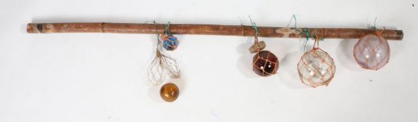 Collection of five coloured glass fishing floats, hung to a cane pole