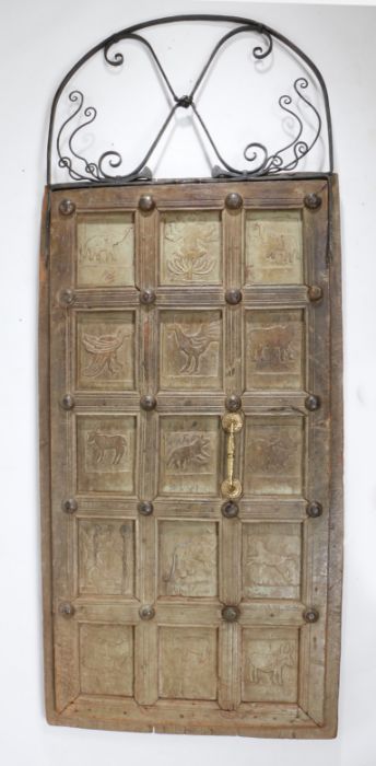 An Indian hardwood door, the wrought iron scrolled arch top above a fifteen panelled door, each