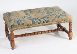 An 18th Century walnut stool, the stuff over verdure tapestry top above turned legs and a turned H