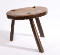 A 19th century elm milking stool, the oval seat raised on three legs, 35cm wide, 29cm high