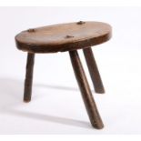 A 19th century elm milking stool, the oval seat raised on three legs, 35cm wide, 29cm high