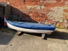 A white painted wooden dinghy, with blue tarpaulin cover