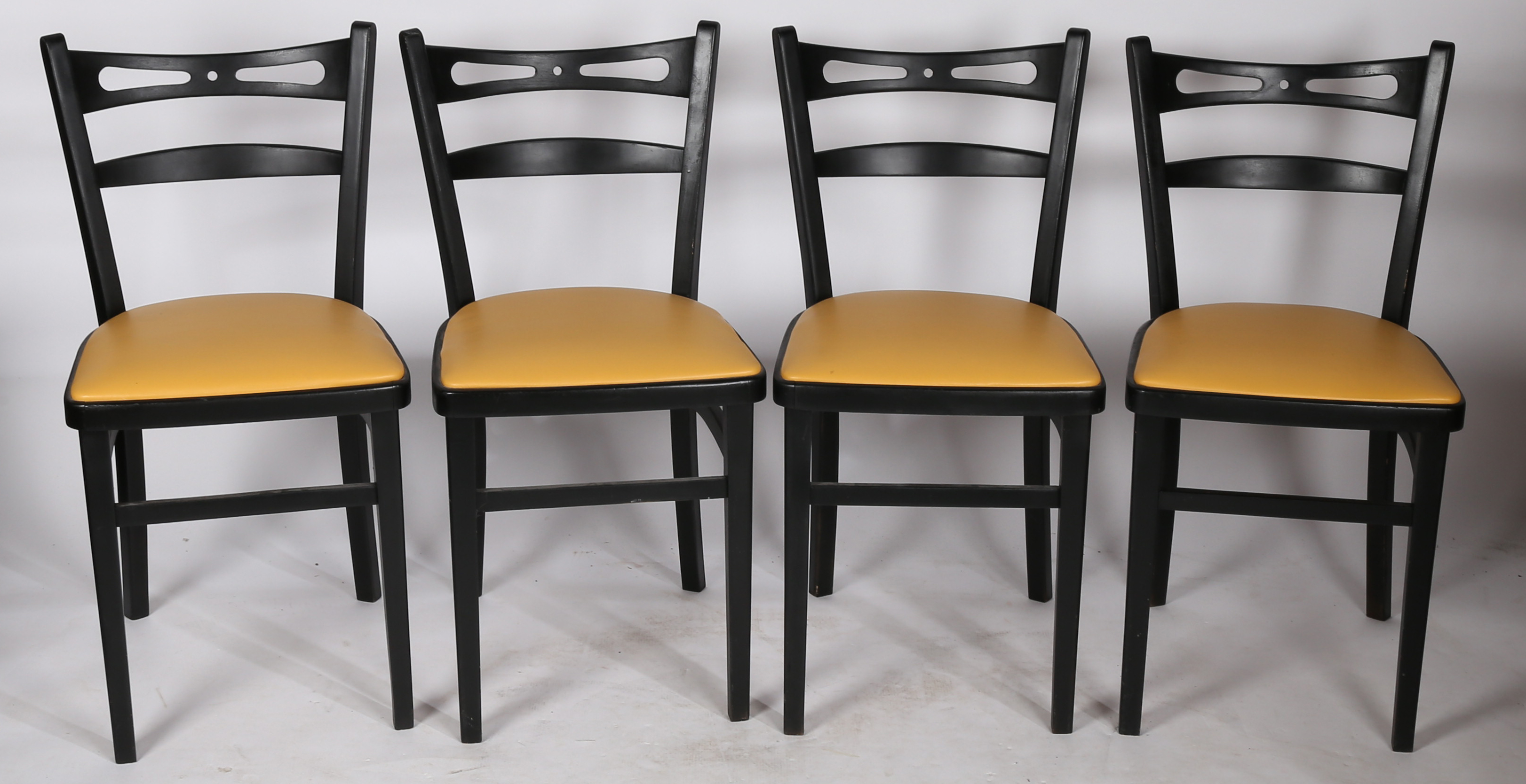 A set of four painted and vinyl upholstered dining chairs in black and tan, stamped to the underside