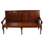 A George III oak settle, the back with five fielded panels above a later plank seat, raised on