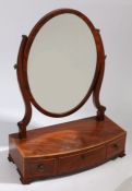 A George III mahogany toilet mirror. the oval mirror raised on a bow-front box base, fitted three