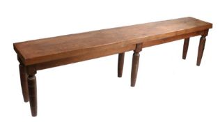 A substantial pine bench, the plank top raised on six turned legs, 249cm wide, 40cm deep, 62cm high