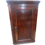 A George III oak hanging corner cupboard, having dental moulded cornice above a panelled door