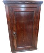 A George III oak hanging corner cupboard, having dental moulded cornice above a panelled door