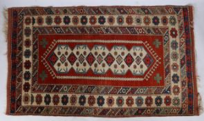 A Caucasian Rug, having a red ground set with central star guls and a hooked design together with