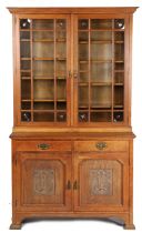 An Arts & Crafts oak glazed bookcase, having a stepped cornice above a pair of glazed doors