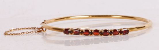 An 18 carat gold and garnet set bracelet, set with seven oval facet cut garnets, the bracelet with