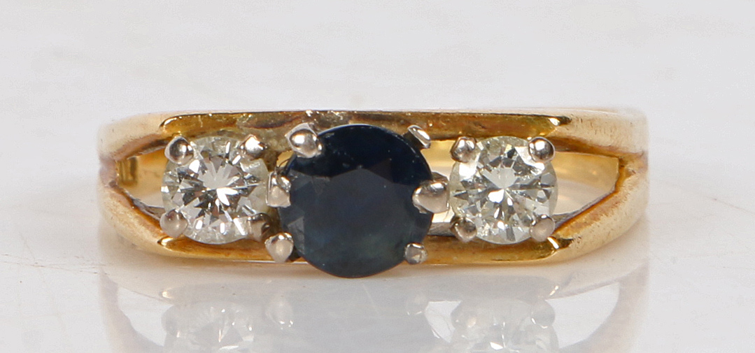 An 18 carat gold sapphire and diamond ring, the central sapphire flanked by two diamonds and pierced