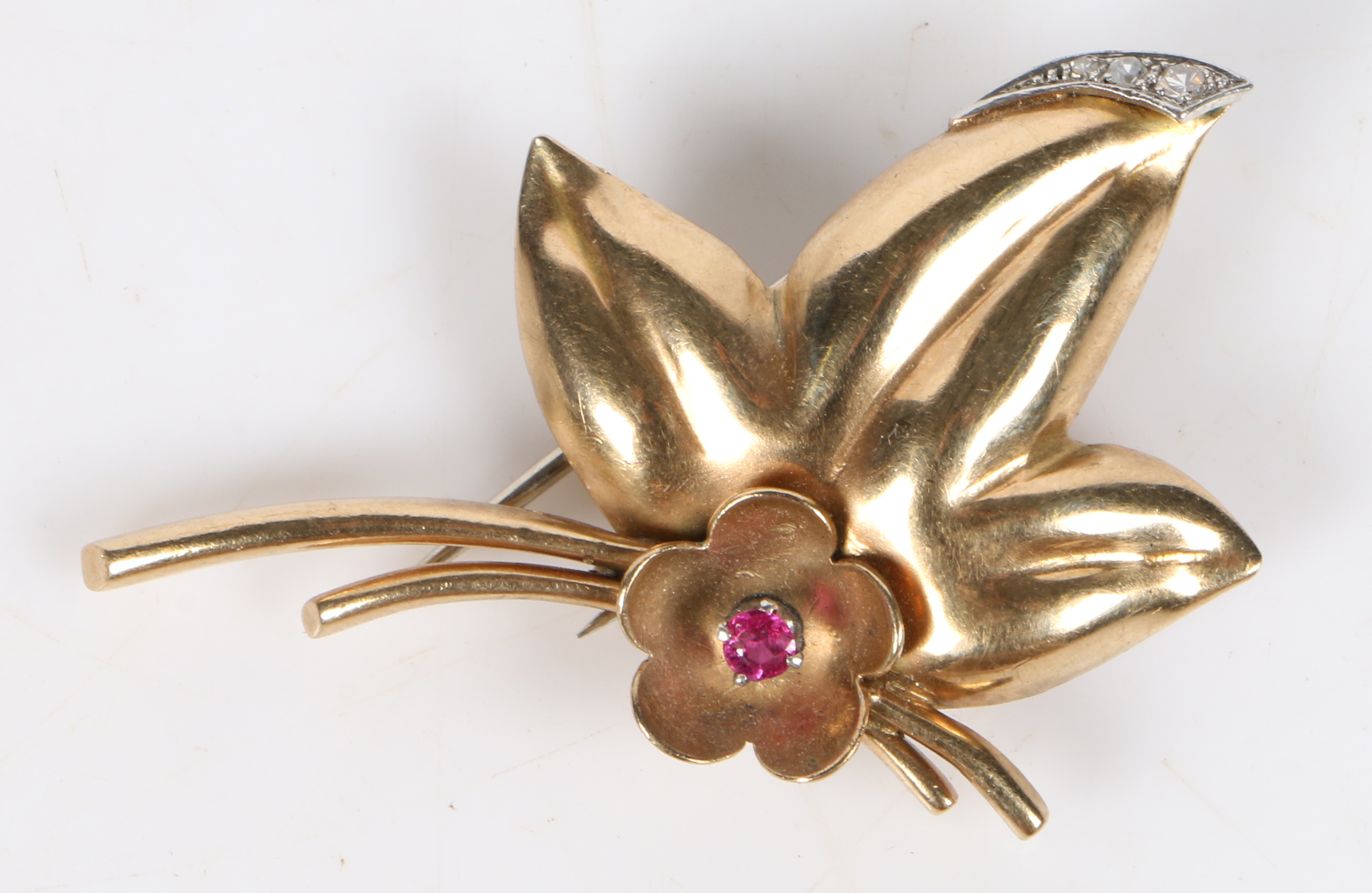 A yellow metal brooch, of foliate form set with a tourmaline to the flower head and three diamonds