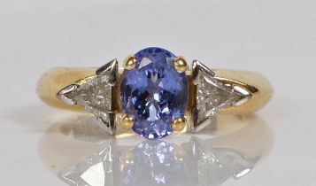 An 18 carat gold, tanzanite and diamond ring, the head set with an oval tanzanite flanked by two