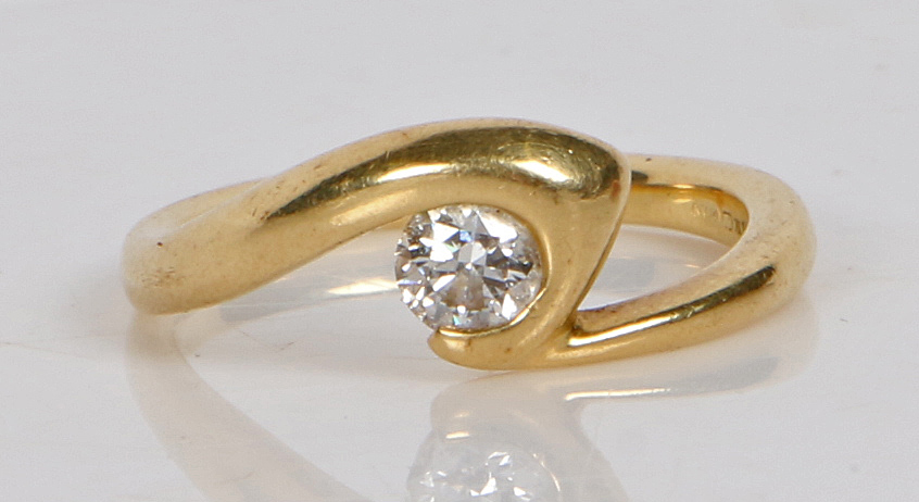 An 18 carat gold and diamond solitaire ring, the crossover band set with a single round brilliant