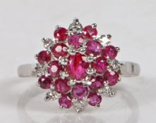 An 18 carat white gold, ruby and diamond cluster ring, the central ruby surrounded by a band of