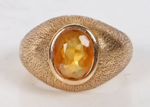 An 18 carat gold and citrine ring, the oval facet cut citrine housed in a beaten effect mount,