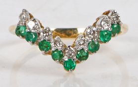 An 18 carat gold, emerald and diamond ring, the V shaped head set with nine round cut emeralds and