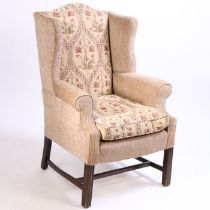 A George III style mahogany wingback armchair, with an arched top above curved arms and channel