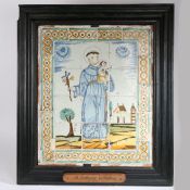 A Delft tile panel depicting Saint Anthony of Padua, housed in a substantial black painted fame with