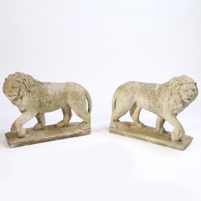 A pair of composite lions, standing position with a foot on a sphere, 69cm long, 56cm high, (2)