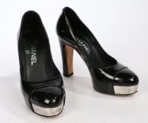 A pair of black patent Chanel heels with platform sole and high heel, silver detailing to the toe.