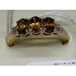 10ct yellow gold ladies ring set with three orange cut stones off set by diamond shoulders. [Ring