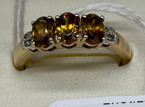 10ct yellow gold ladies ring set with three orange cut stones off set by diamond shoulders. [Ring