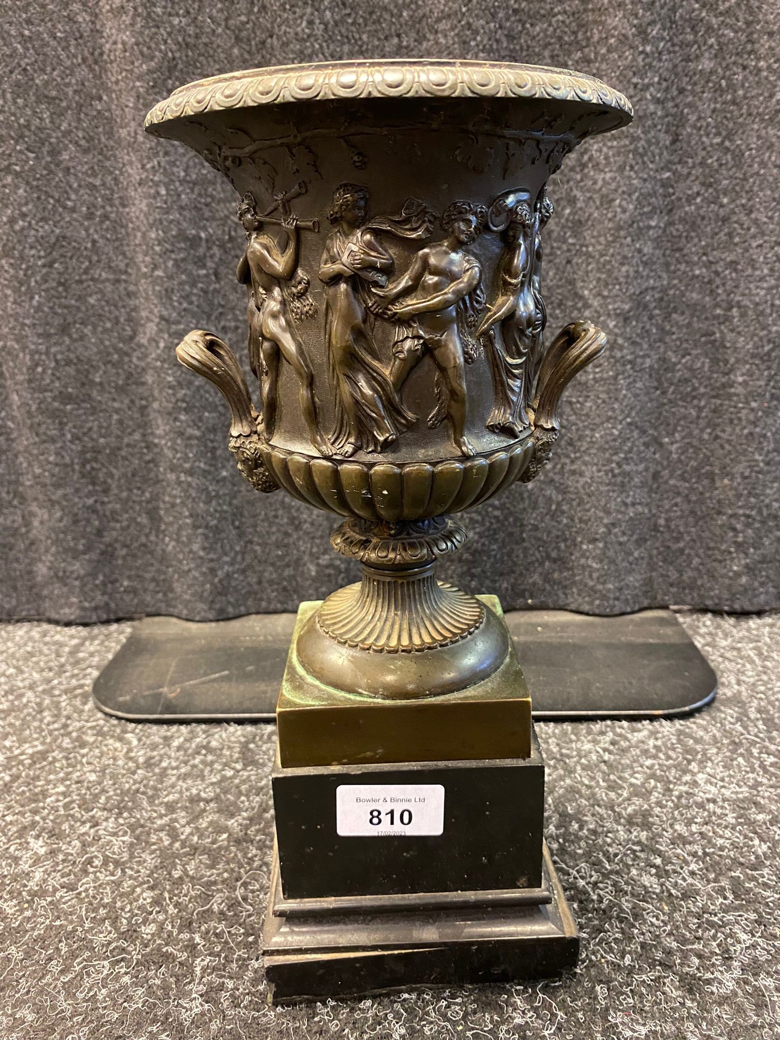 Antique bronze urn sat upon a slate base. Designed with Greek figures. [31.5cm high]