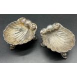 A Pair of Birmingham silver shell design salt dishes, Supported on three fish design legs. [3.