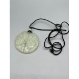 A Jade panel pendant of circular form, with cord necklace.