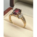 9ct yellow gold ladies ring set with a red topaz stone off set by diamond stone shoulders. [Ring