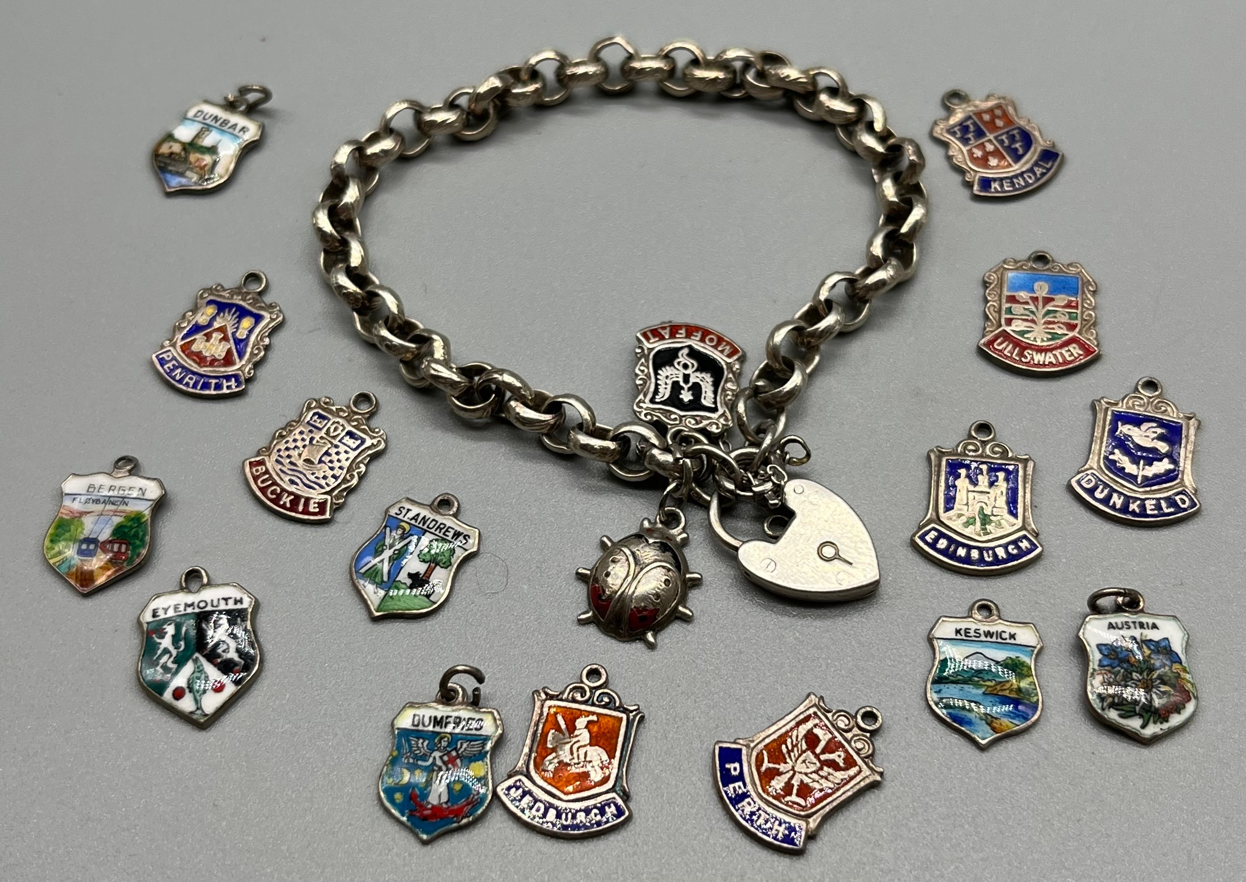 Silver charm bracelet together with silver and enamel souvenir shield fobs.