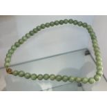 Chinese green jade bead necklace fitted with a gold tone clasp and catch. [Tested as gold]