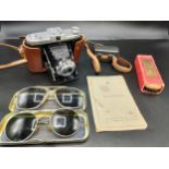 A tray containing vintage sunglasses and zeiss ikon nettar camera.