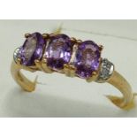 9ct yellow gold ring set with three purple topaz stones off set by diamond shoulders. [Ring size