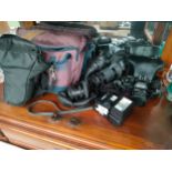 A shelf of camera equipment and accessories to include Ricoh KR-10 camera, lenses and carry cases