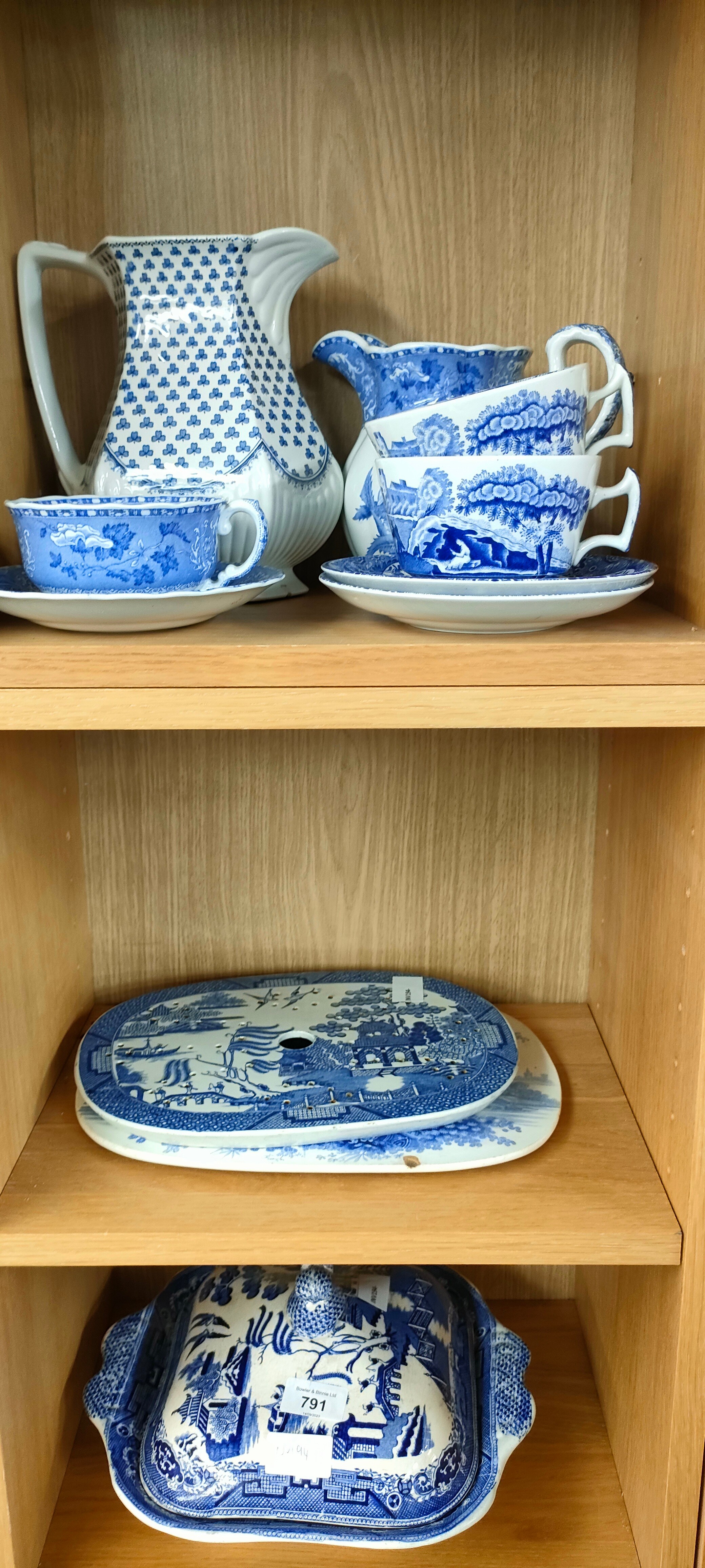 Three shelves of blue and white wares; lidded tureen, Willow pattern drip dish and Spode cups and