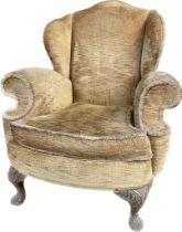 A antique wing back armchair with raised carved legs