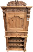 Pine wine unit, a cupboard door and rack surmounted by carved foliate and grape design