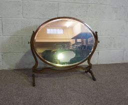 An Edwardian oval mirror on stand, with carved supports, 73cm high, 82cm wide; and another oval
